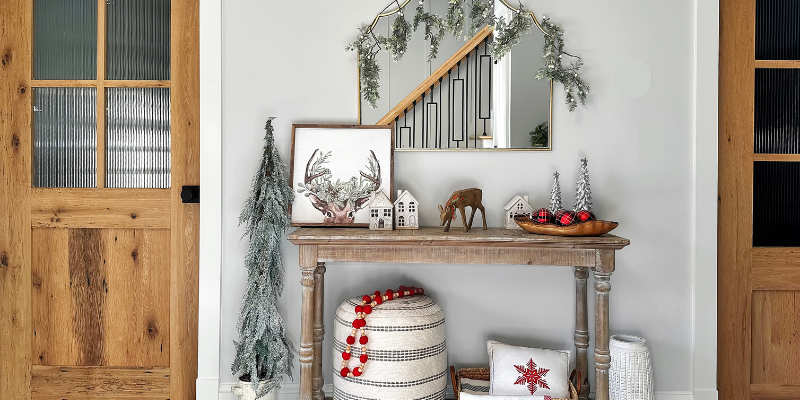 console table decor, christmas decor ideas, holiday console table, holiday entryway, deer print, ceramic christmas houses, live edge olivewood bowl, wool blend throw, snowflake pillow, deer print, vintage garland, vintage ornaments, braided basket, textured pouf, resin christmas trees, resin reindeer, terracotta vase, artificial hgtv tree, target white berry garland