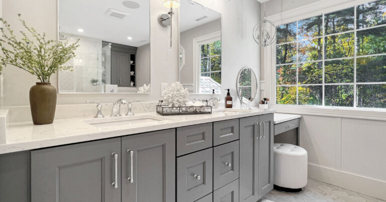 Light and airy primary bathroom renovationwith a double vanity in a blue/gray paint color with white stone countertops, a makeup vanity, and a walk-in shower with three showerhead options.