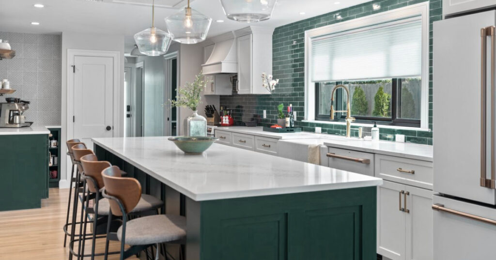 An elegant kitchen with deep emerald green cabinets paired with sleek white quartz countertops. A glossy green subway tile backsplash adds a pop of color, complemented by brass fixtures and pendant lighting over the kitchen island.