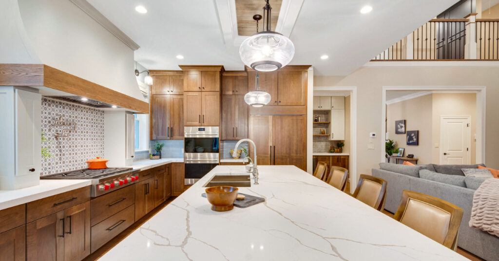 A rustic modern kitchen with rich wood cabinetry, a large kitchen island with white quartz countertops, and a bold patterned backsplash. The space is illuminated by globe pendant lights, creating a warm, inviting environment.