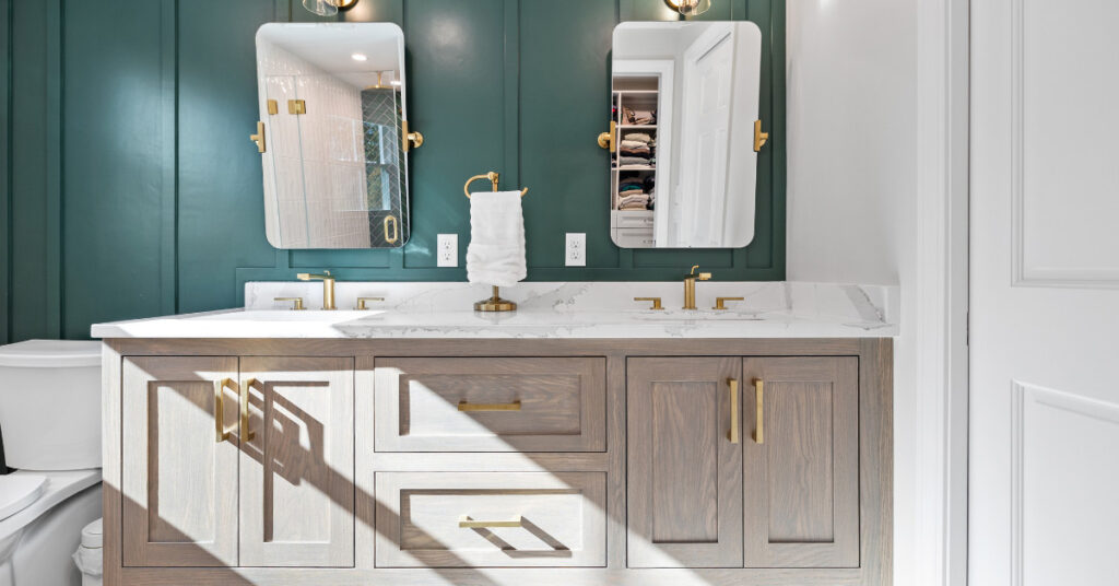 Modern double vanity with gold fixtures, quartz countertop, and green accent wall in a primary bathroom.