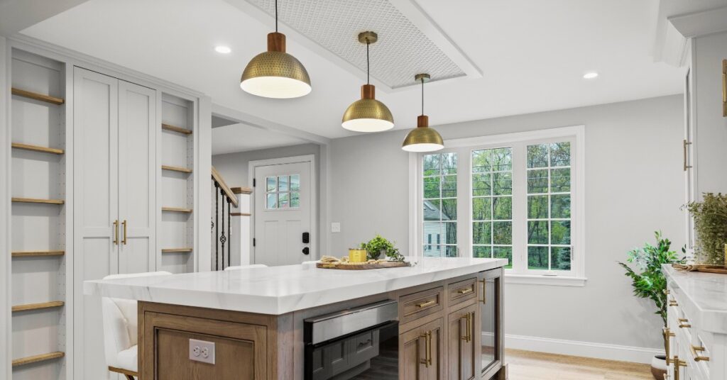 Modern kitchen with Elyona pendant lights above a wood kitchen island featuring white quartz countertops, brass hardware, and custom cabinetry.