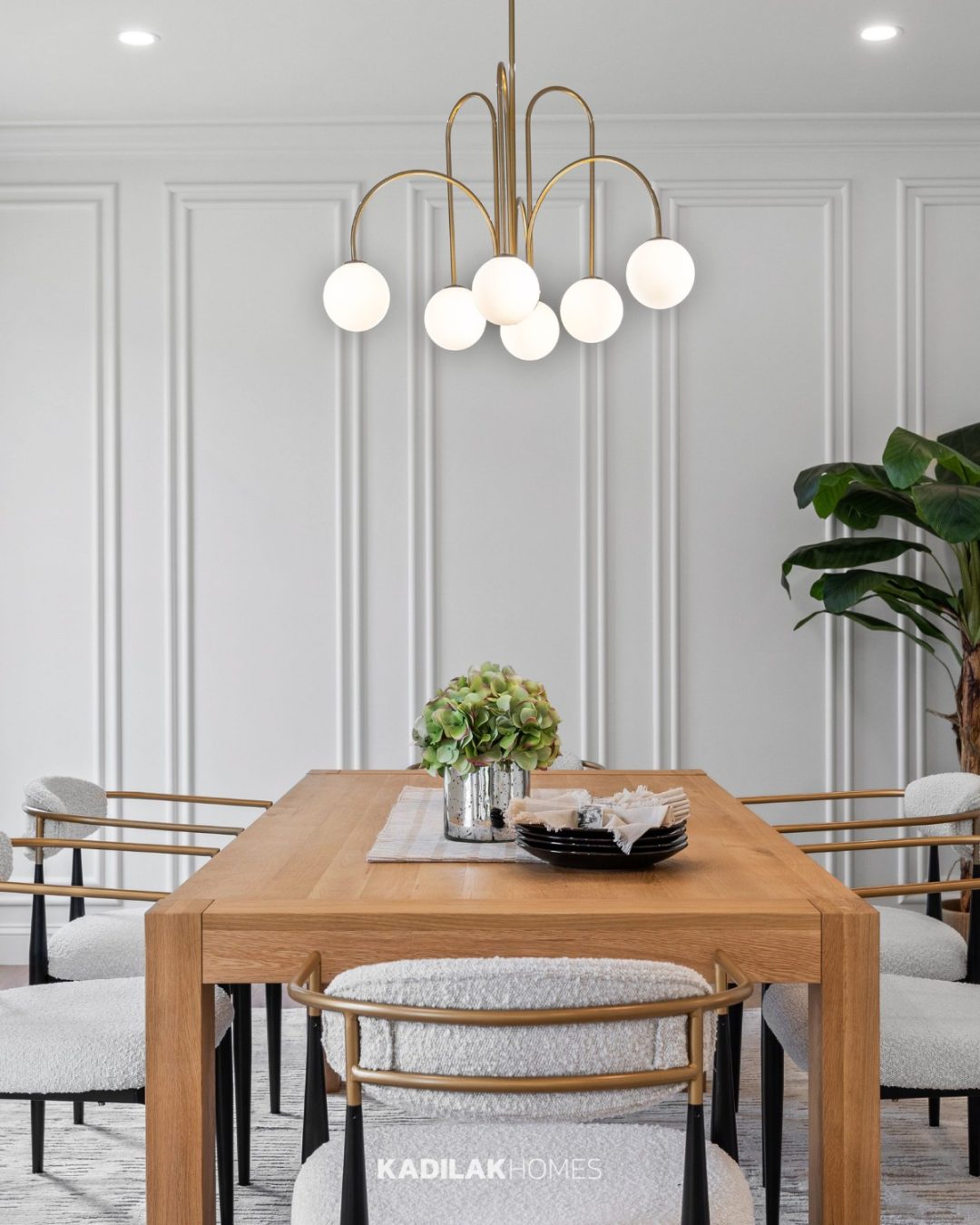 Bradrick Globe Chandelier with a warm brass finish and opal glass globe shades hanging above a modern wood dining table.