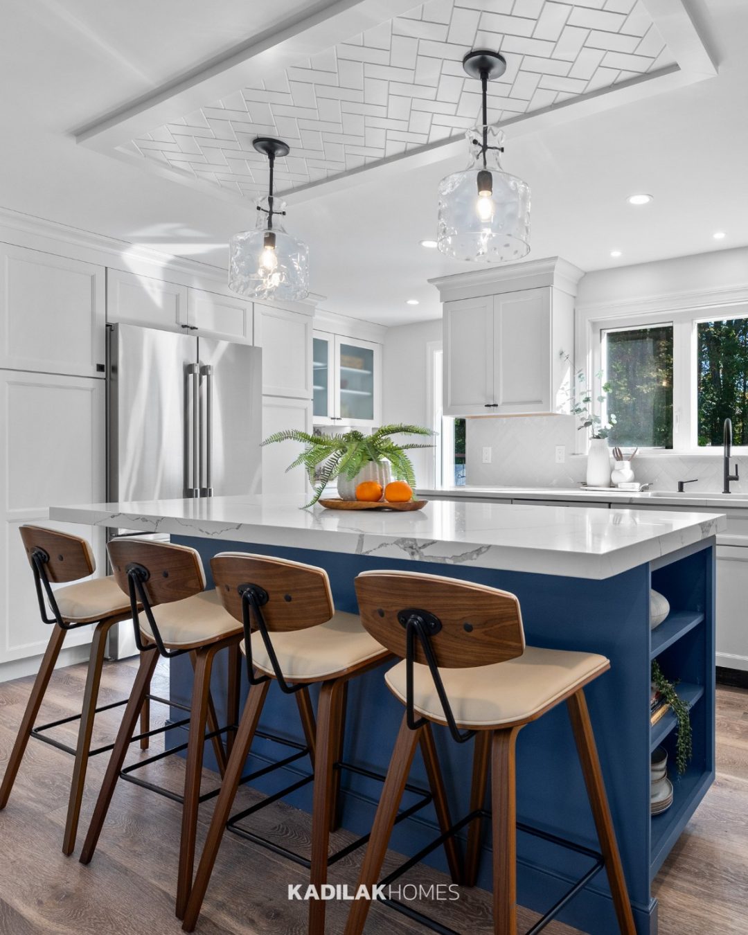 Santorini 4-Light Pendant by Millennium Lighting with clear textured glass shades hanging above a blue kitchen island in a modern white kitchen.