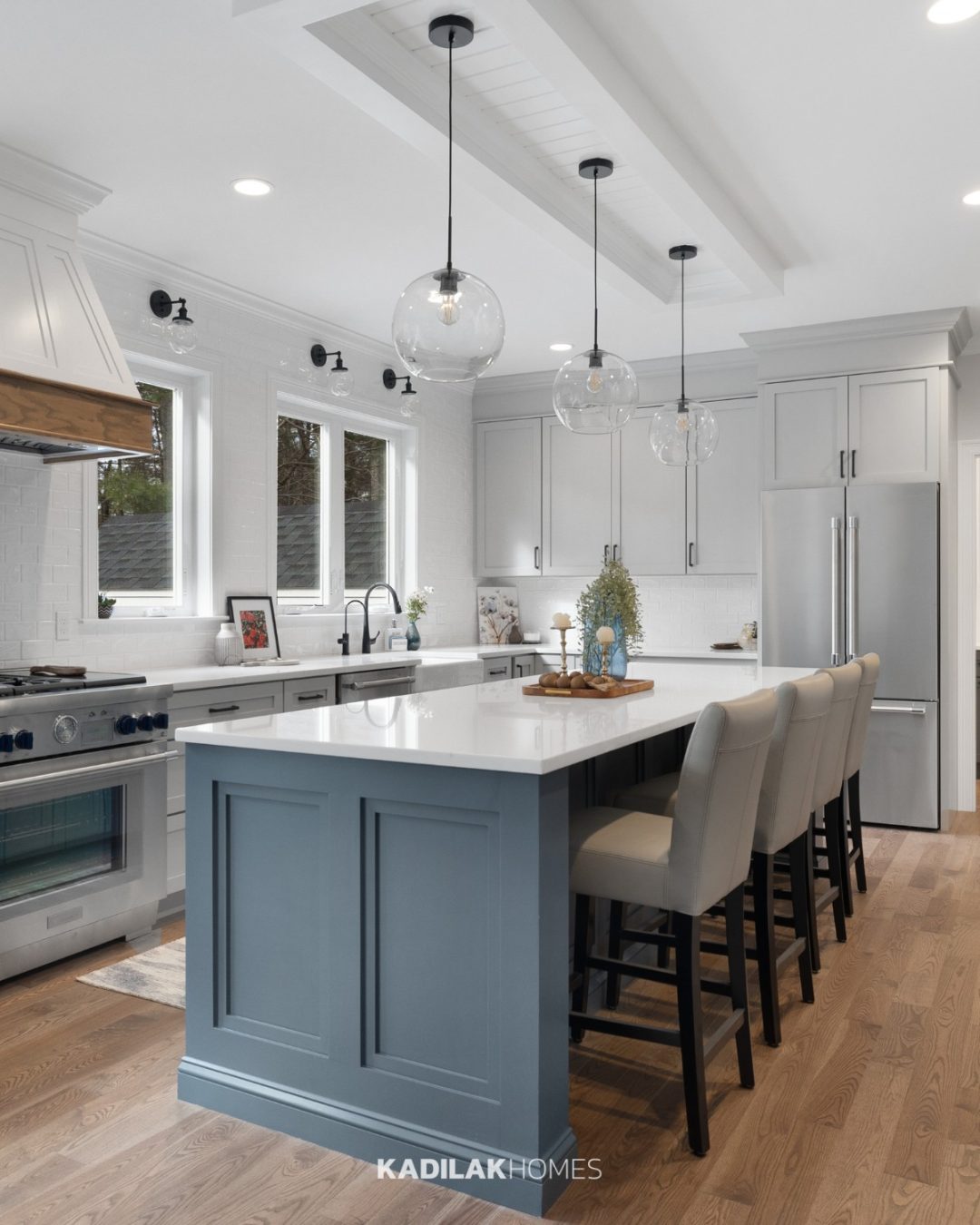 Avell Pendant by Millennium Lighting with clear glass globe shades hanging above a blue kitchen island in a modern farmhouse kitchen.