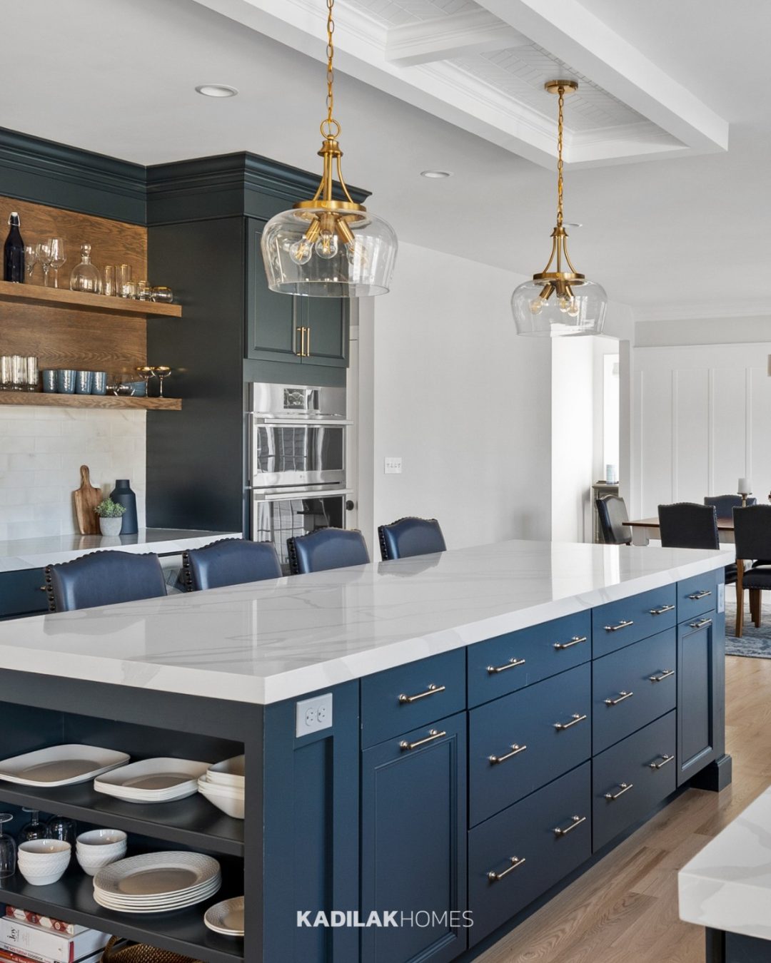 Breena Dome Pendant by Birch Lane with a clear glass shade and warm brass finish hanging above a navy blue kitchen island.