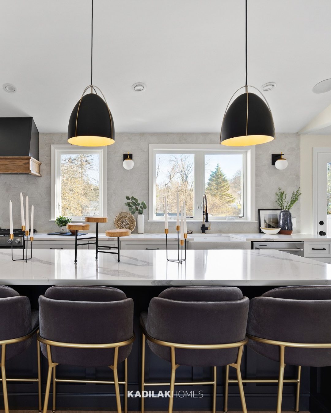 Norman Pendant by Generation Lighting in a black finish with brass accents hanging above a modern kitchen island with white quartz countertops.