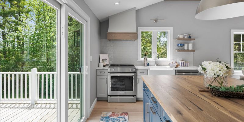 kitchen renovation ideas with square island with single pendant. Reclaimed wood countertop on island. Navy blue island cabinets. Curved range hood. Vaulted ceilings with oak beams. Open concept kitchen and living room.