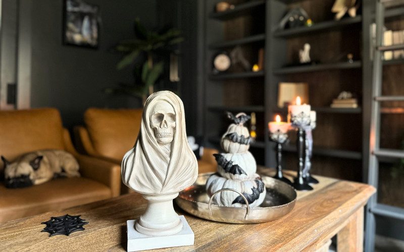 A skull-shaped candle holder, cobweb-shaped coasters, and flickering LED candles on a coffee table in a Halloween-themed library.