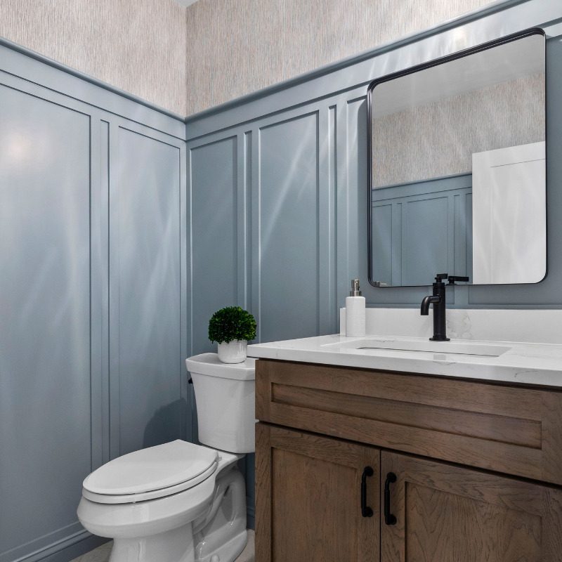 Powder Room bathroom design with extra tall wainscoting in Kentucky Haze by Benjamin Moore, a dusty baby blue paint color. Paired with a white oak bathroom vanity, matte black hardware, and grasscloth wallpaper.