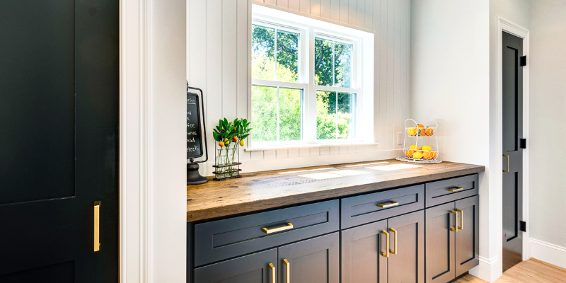 Navy Blue pantry cabinets with white shiplap walls, brushed gold hardware, reclaimed wood countertop, and a small window