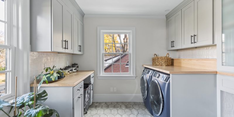 Vintage inspired laundry room with provenzal alhama grey procelain floor tile, oak countertops over washer and dryer, and laundry cabinets