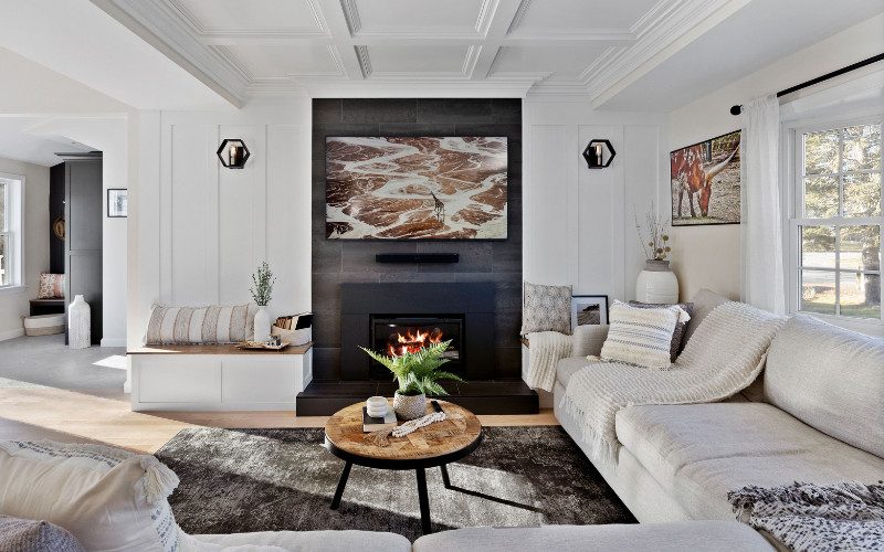A cozy modern living room featuring a sleek fireplace, neutral-colored seating, and layered textures with plush throw pillows and blankets, adding warmth and softness to the minimalist design.