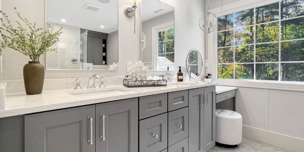 Light and airy primary bathroom renovationwith a double vanity in a blue/gray paint color with white stone countertops, a makeup vanity, and a walk-in shower with three showerhead options.
