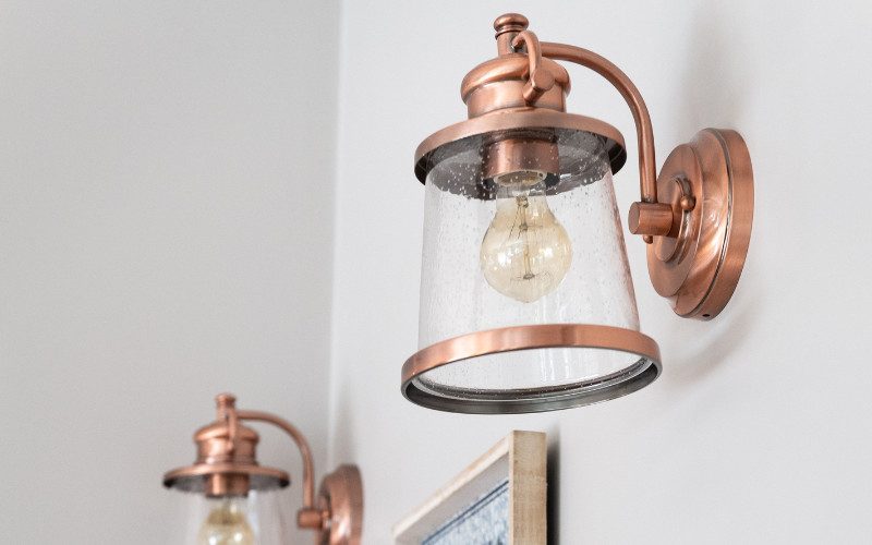 Close-up of two copper wall sconces with glass shades, highlighting warm metallic accents in a modern home.