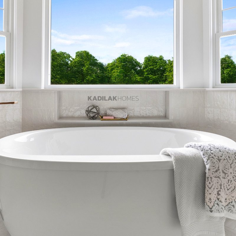 Freestanding soaking tub with built-in storage shelf under a large window, surrounded by natural light.