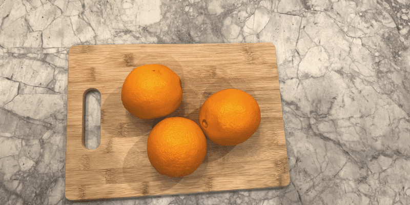 3 whole oranges on a bamboo cutting board with super white quartzite counters
