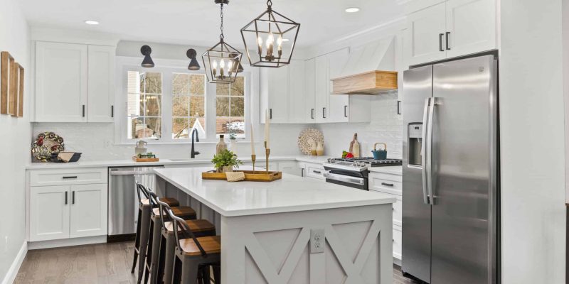 Gray kitchen island with double X design, white hood with wood trim, triple casement window over sink