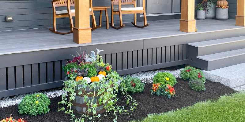 fall front porch ideas, dark house with black trim, porch with wood posts, porch with wood columns, hardie plank siding, house with black windows, front porch idea, cozy outdoor seating, pumpkin decor, front door with wreath, fall wreath ideas, set of planters, sitting area, west elm planter, wood outdoor rocking chairs, porch landscaping ideas with barrel, green artiscapes landscaping billerica ma
