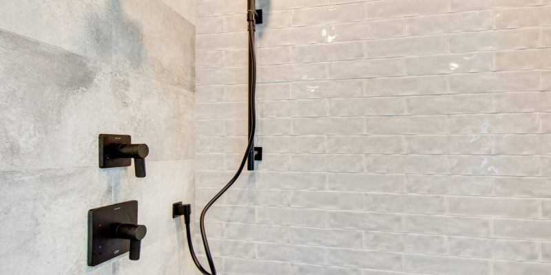A classic and timeless shower design inside the primary en suite with an off white textured subway tile, all black shower trim and hardware, and four different shower heads including a rainfall shower head. A large walk-in shower with floor to ceiling glass doors.