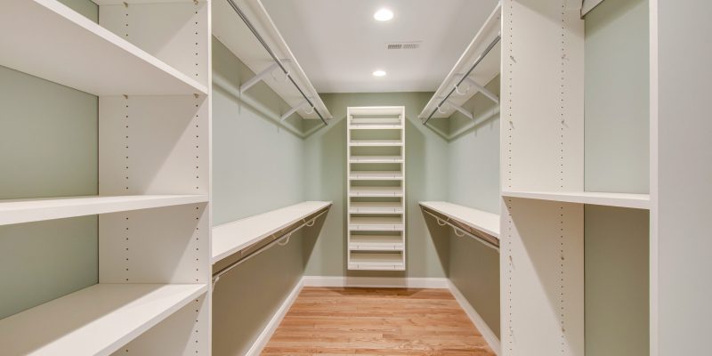 Primary suite walk-in closet with floor to ceiling built-ins including built-in shelving storage, hanging rods, and shoe racks.