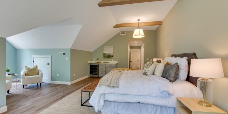 Primary suite with high vaulted ceilings, wood beams, sage green walls, and a mini bar with a fridge, sink, and a sitting area.