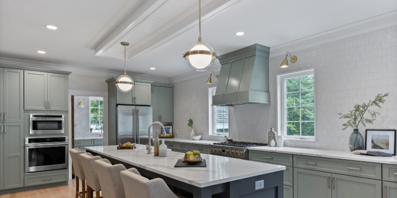 Light green kitchen cabinets with dark gray island, kitchen island with turned legs, sink in kitchen island, coffered ceiling over kitchen island, coffered ceiling ideas