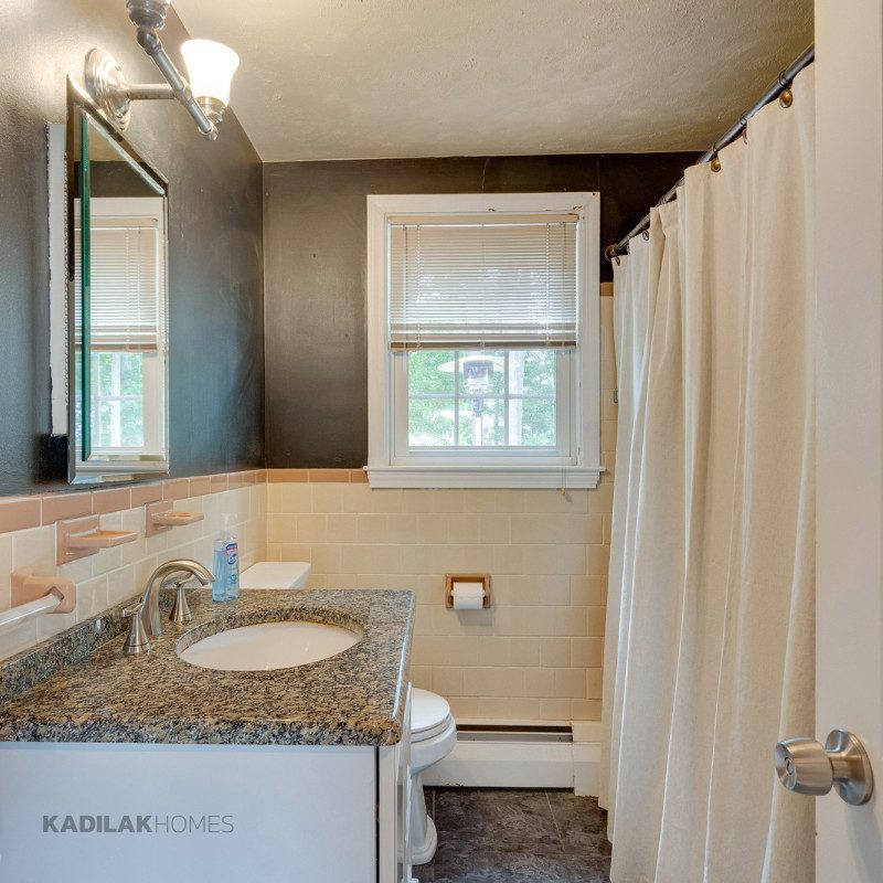 Before bathroom renovation with dark walls, beige tile, small vanity, and outdated finishes in a 1958 Cape style home.