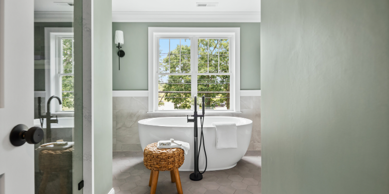 primary bathroom with freestanding soaking tub in front of window and floor mounted faucet, sconces flanking windows