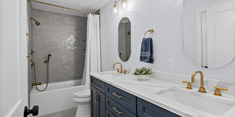 bathroom with blue cabinets, warm taupe tile, brushed gold fixtures