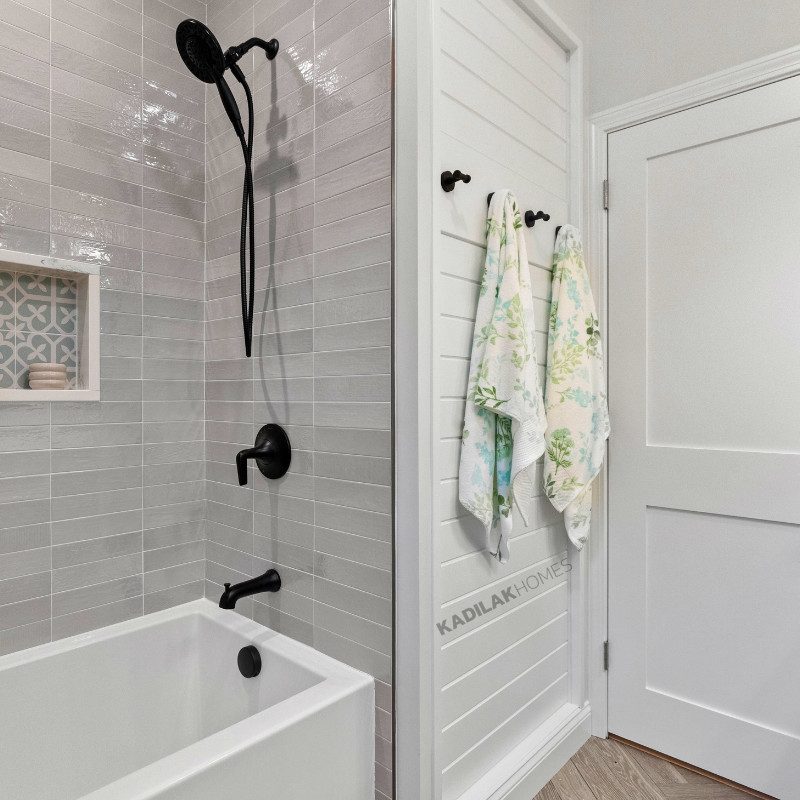 Small bathroom with vertical towel hooks mounted on white shiplap wall next to a shower with matte black fixtures.