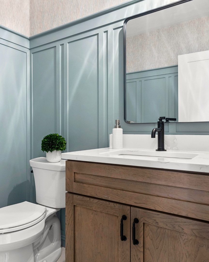 Bathroom with Kentucky Haze blue green wainscoting and grasscloth wallpaper above, featuring wood vanity and black fixtures in a soft coastal home aesthetic