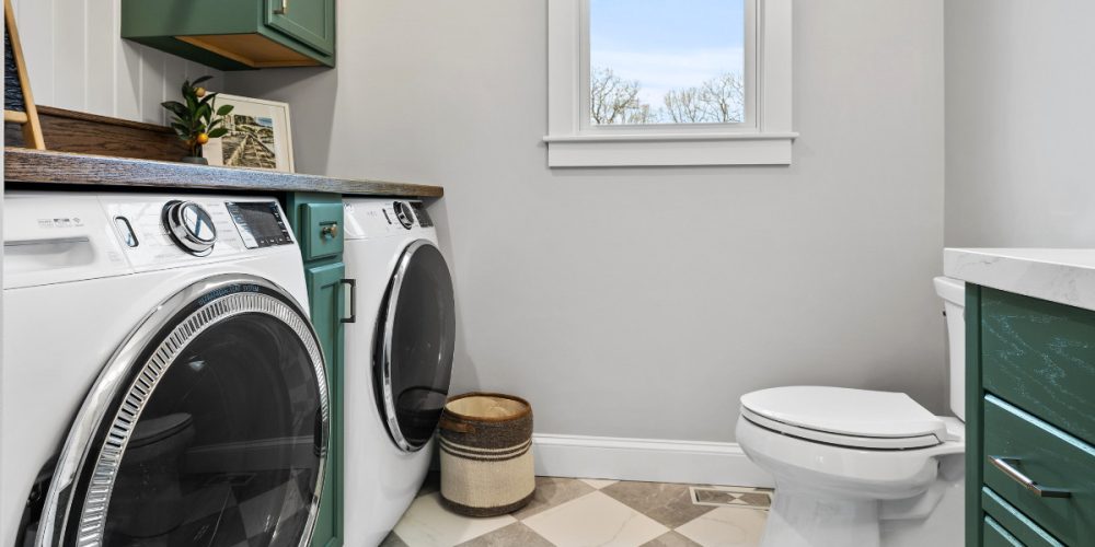 Laundry room with cabinets painted in Benjamin Moore Gothic Green, wood countertop, and a checkerboard tile floor by Kadilak Homes.