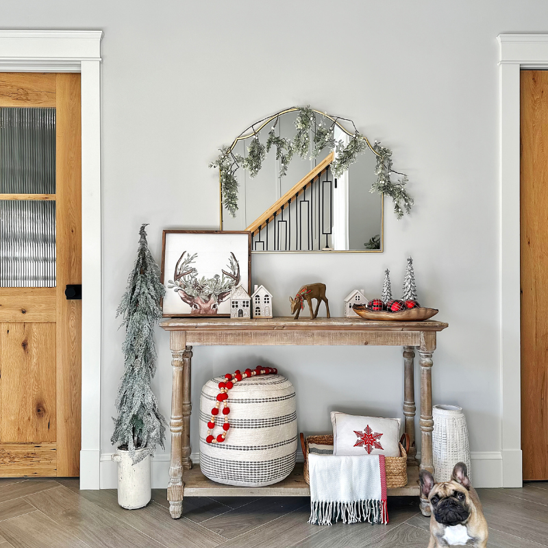 Our french bulldog Luna posing in front of our console table decorated for the holidays! Featuring a reindeer art print, ceramic Christmas houses, a live edge olive wood bowl, a wool blend throw, a snowflake throw pillow, vintage garland, vintage ornaments, a braided basket, textured pouf, resin Christmas trees, terracotta vase, artificial HGTV tree, and white berry garland from Target!