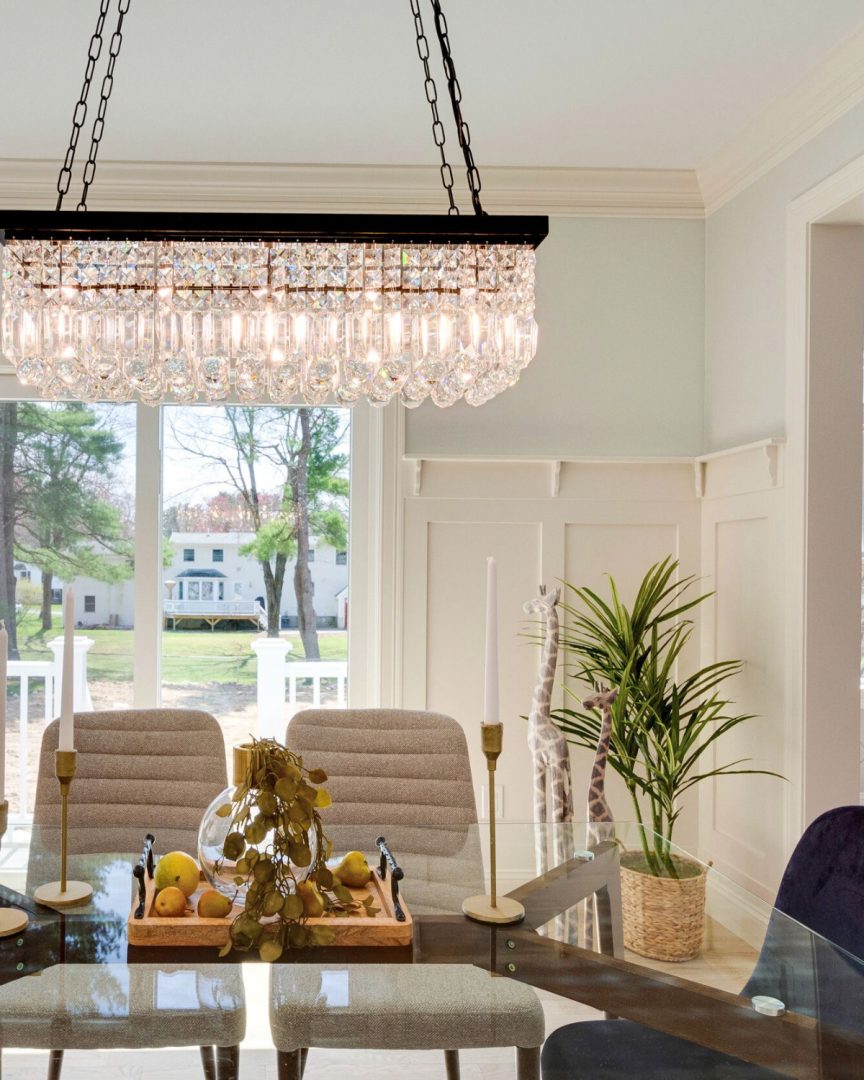 Dining room with Oystershell 864 by Benjamin Moore featuring soft beige walls, wainscoting, crystal chandelier, and a light-filled coastal home aesthetic
