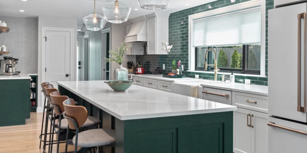 An elegant kitchen with deep emerald green cabinets paired with sleek white quartz countertops. A glossy green subway tile backsplash adds a pop of color, complemented by brass fixtures and pendant lighting over the kitchen island.