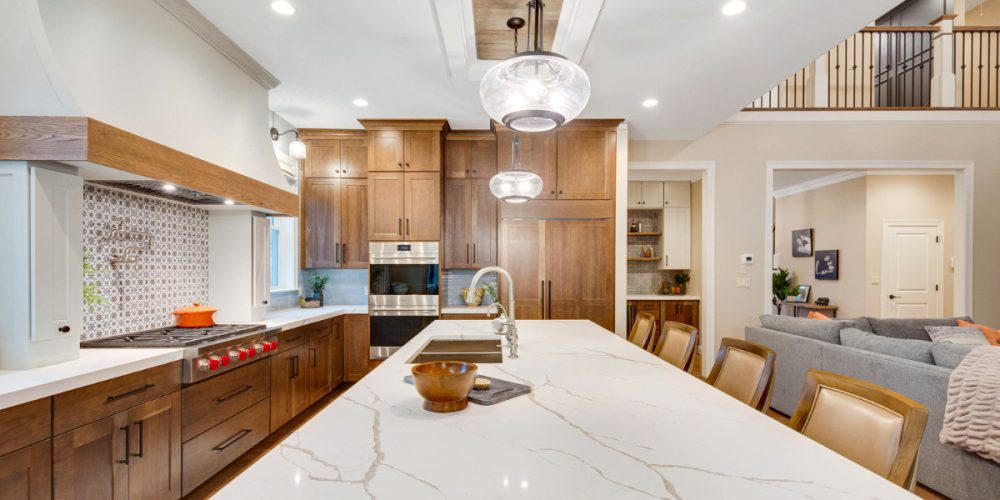 A rustic modern kitchen with rich wood cabinetry, a large kitchen island with white quartz countertops, and a bold patterned backsplash. The space is illuminated by globe pendant lights, creating a warm, inviting environment.
