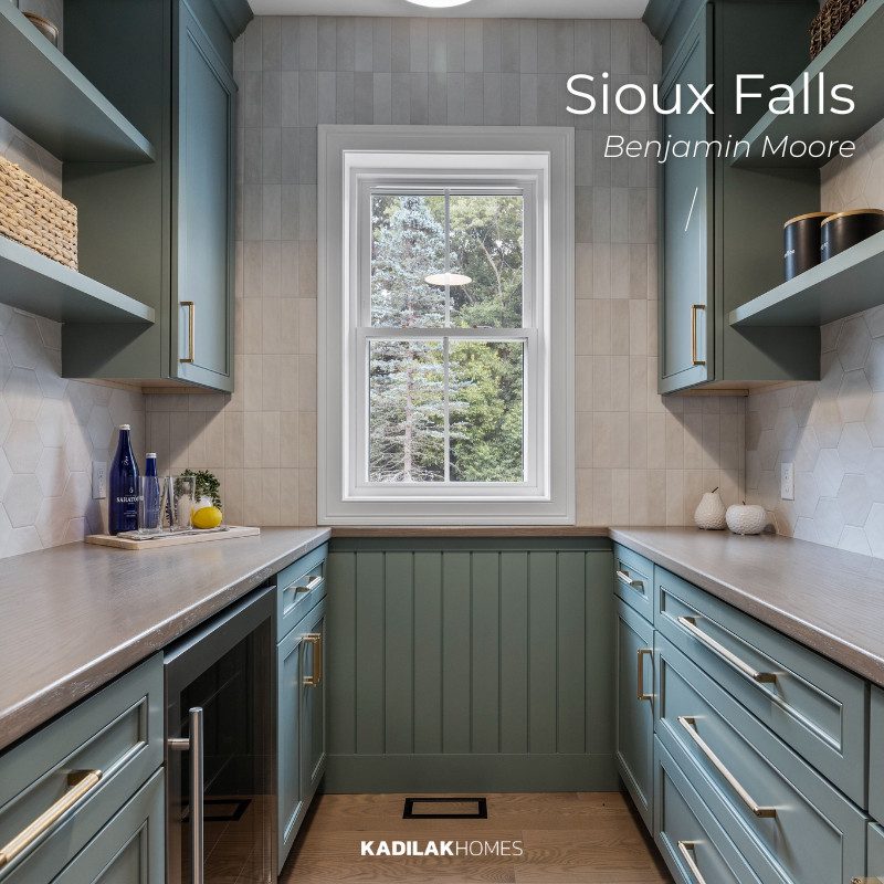 Stylish pantry featuring Benjamin Moore Sioux Falls, a rich, earthy green with blue-gray undertones. The custom cabinetry, paired with warm wood countertops, brass hardware, and textured tile backsplash, creates a sophisticated yet cozy kitchen design with an earthy neutral color palette for home.