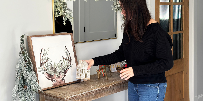 console table decor, christmas decor ideas, holiday console table, holiday entryway, deer print, ceramic christmas houses, live edge olivewood bowl, wool blend throw, snowflake pillow, deer print, vintage garland, vintage ornaments, braided basket, textured pouf, resin christmas trees, resin reindeer, terracotta vase, artificial hgtv tree, target white berry garland