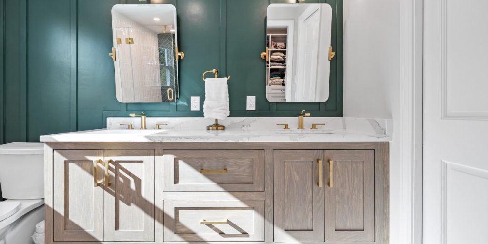 Modern double vanity with gold fixtures, quartz countertop, and green accent wall in a primary bathroom.