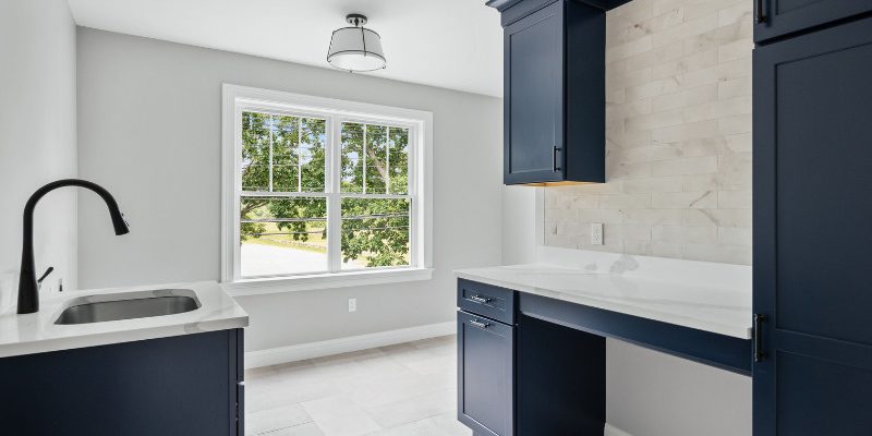Laundry room with cabinets painted in Benjamin Moore Navy Masterpiece, white utility sink, and neutral tile backsplash, designed by Kadilak Homes.