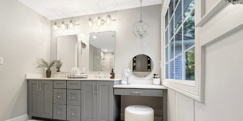 Long double vanity with sconces, double vanity with drop down make-up counter, vanity with chandelier, bathroom with chrome fixtures, large picture window in bathroom, benjamin moore bathroom walls Shoreline 1471, Sherwin Williams Serious Gray cabinets