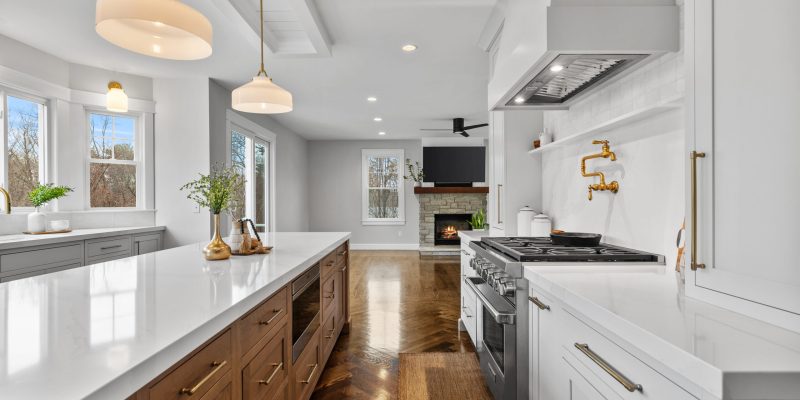 1990s maple kitchen, small kitchen, small island, cramped kitchen layout, kitchen with angled bay and slider, kohler artifacts pot filler, shelf under range hood, quartz backsplash, stone backsplash, tall cabinets on either side of stove