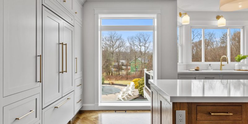 kitchen with oak wood island, paneled appliances, inset cabinets, neutral color scheme, henry sconces, henry pendants, odd shaped kitchen, weird kitchen layout, kitchen sink in bay, large picture window, benjamin moore Cloud Cover OC-25, kohler artifacts kitchen faucet, kohler artifacts bar faucet, dramatic floor to ceiling window