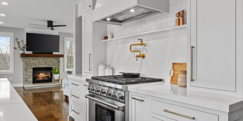 1990s maple kitchen, small kitchen, small island, cramped kitchen layout, kitchen with angled bay and slider, kohler artifacts pot filler, shelf under range hood, quartz backsplash, stone backsplash, tall cabinets on either side of stove