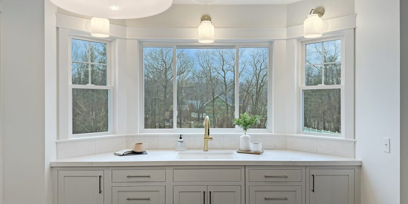 kitchen with oak wood island, paneled appliances, inset cabinets, neutral color scheme, henry sconces, henry pendants, odd shaped kitchen, weird kitchen layout, kitchen sink in bay, large picture window, benjamin moore Cloud Cover OC-25, kohler artifacts kitchen faucet, kohler artifacts bar faucet, kitchen with large picture window over sink
