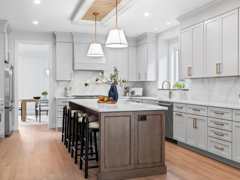 Modern kitchen with Benjamin Moore Pale Oak cabinets, a large wooden island with seating, quartz countertops, and brass hardware. The kitchen features a marble backsplash, stainless steel appliances, and pendant lighting over the island. A unique oak shiplap ceiling detail adds warmth to the space.