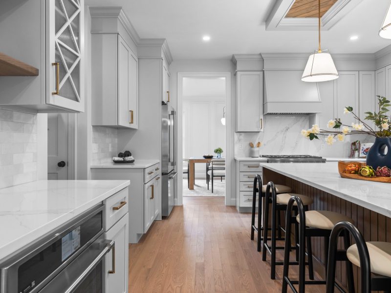 Modern kitchen with Benjamin Moore Pale Oak cabinets, quartz countertops, and brass hardware. The kitchen features a large wooden island with seating, stainless steel appliances, a marble backsplash, and a unique ceiling design with oak shiplap and pendant lighting.