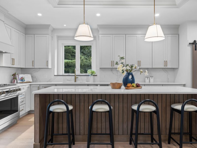 Modern kitchen featuring Benjamin Moore Pale Oak cabinets, a large wooden island with seating, quartz countertops, and brass hardware. The design includes stainless steel appliances, a marble backsplash, pendant lighting, and a barn-style sliding door leading to the pantry.
