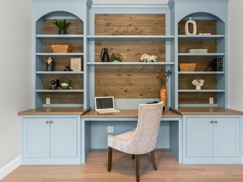 Built-in home office desk and shelving unit painted in Benjamin Moore Kentucky Haze AC-16, featuring wood paneling, open shelving, and light wood countertops. The space includes minimalist decor and a cozy upholstered chair, creating a functional and stylish workspace.